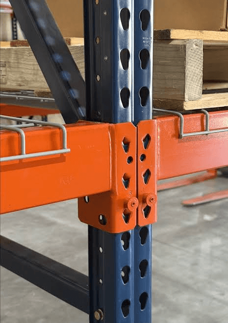 Close-up of orange pallet rack beams connected to a blue teardrop upright with wire decking